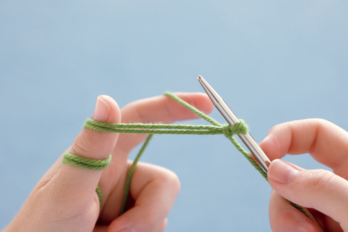 Hold the yarn in slingshot position, with the single strand (the one connected to the ball of yarn) going over your index finger. Take the double-strand tail and loop it, counterclockwise, twice around your thumb.